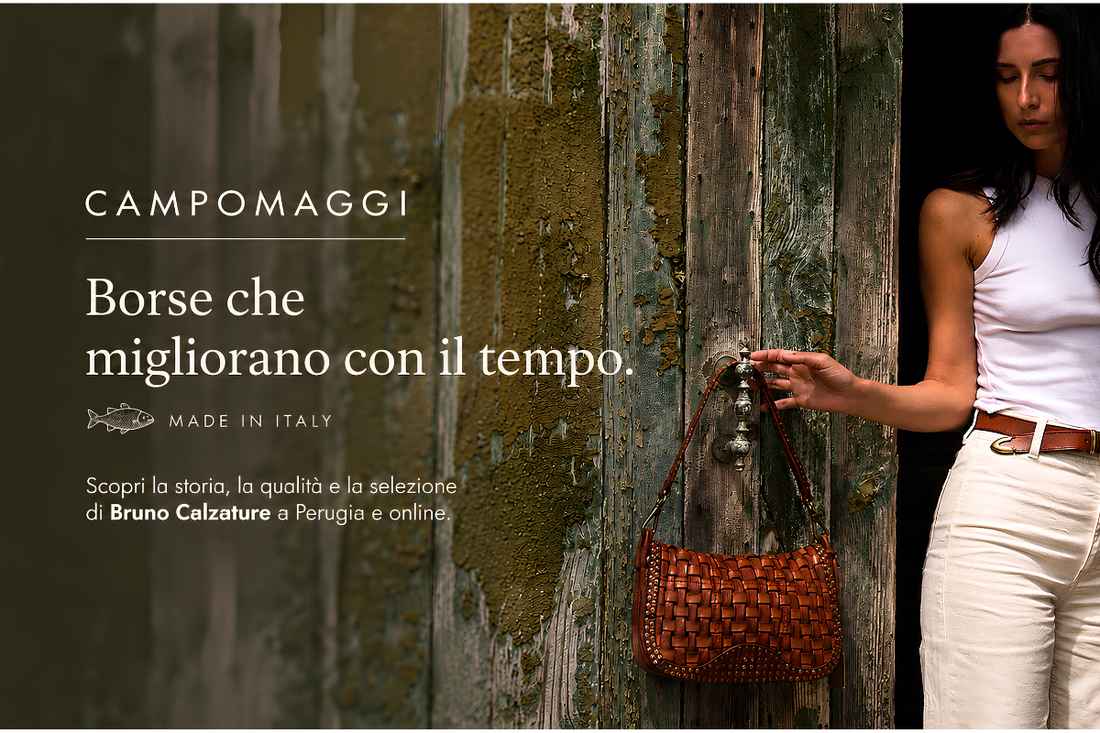 Donna con una borsa Campomaggi in pelle intrecciata davanti a un portone in legno. Immagine di copertina dell'articolo dedicato alla storia, alla qualità e all'artigianalità delle borse Campomaggi.