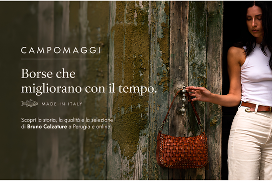 Donna con una borsa Campomaggi in pelle intrecciata davanti a un portone in legno. Immagine di copertina dell'articolo dedicato alla storia, alla qualità e all'artigianalità delle borse Campomaggi.