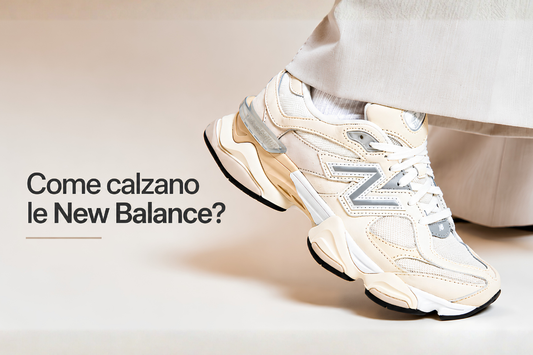 Sneaker New Balance beige e bianca indossata con pantalone chiaro, fotografata in stile editoriale minimal con testo “Come calzano le New Balance?” su sfondo neutro chiaro.